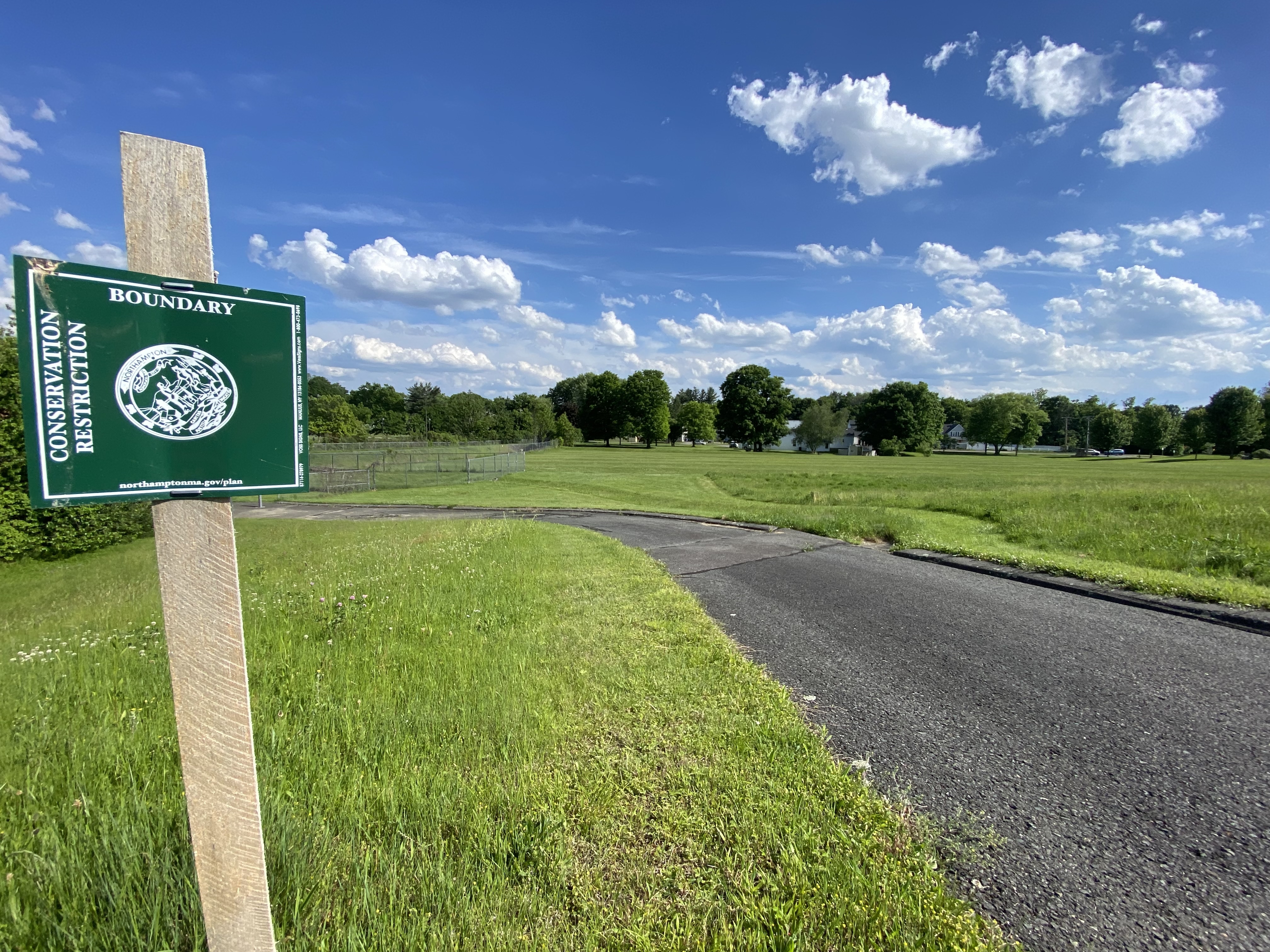 Bear Hill field, a grassy, mowed field, is seen in the background. In the foreground, a small "conservation restriction" sign is the only signage that acknowledges its existence.