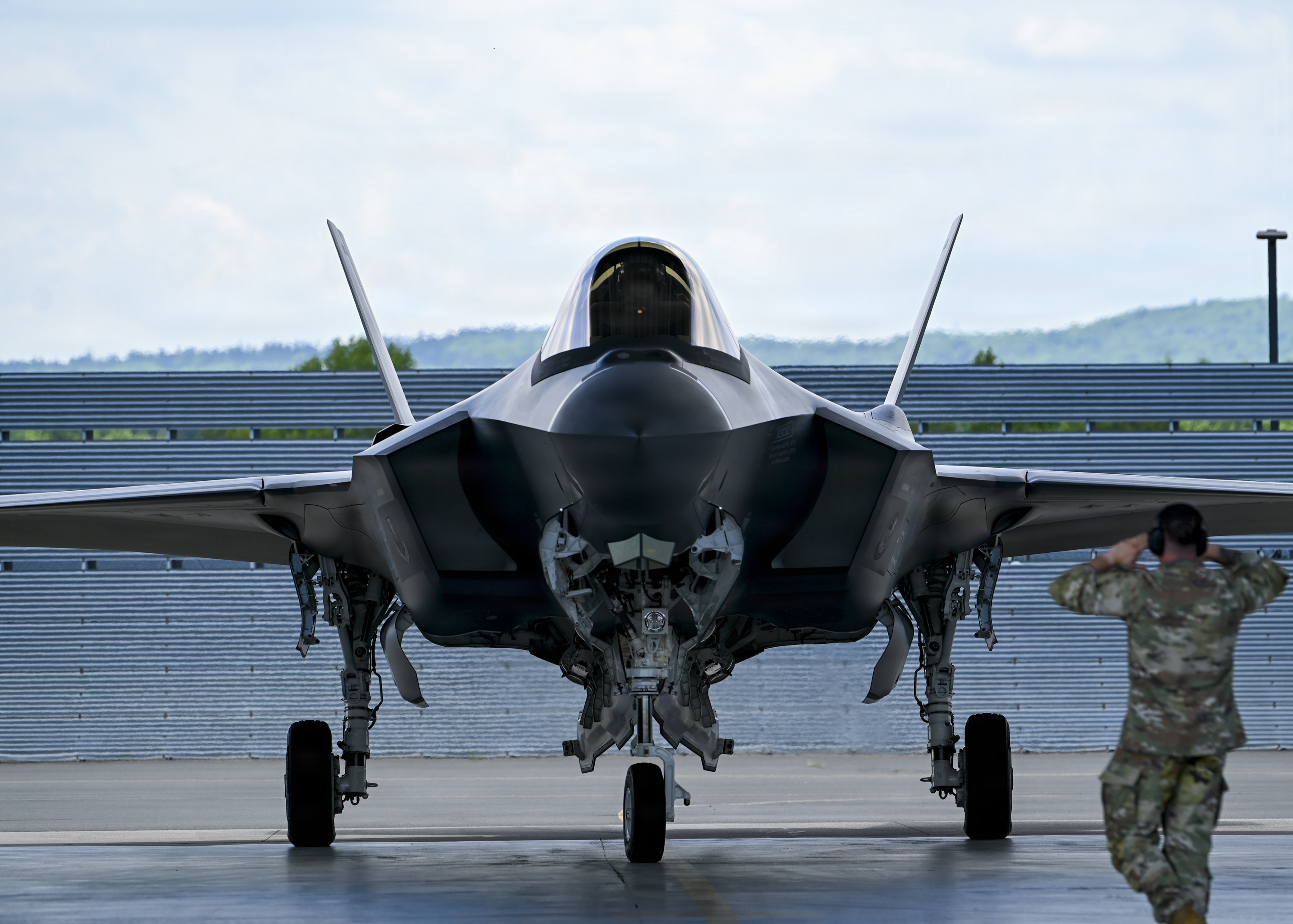 A black F-35 fighter jet faces ahead while a crew chief, dressed in camouflage, stands in front motioning.