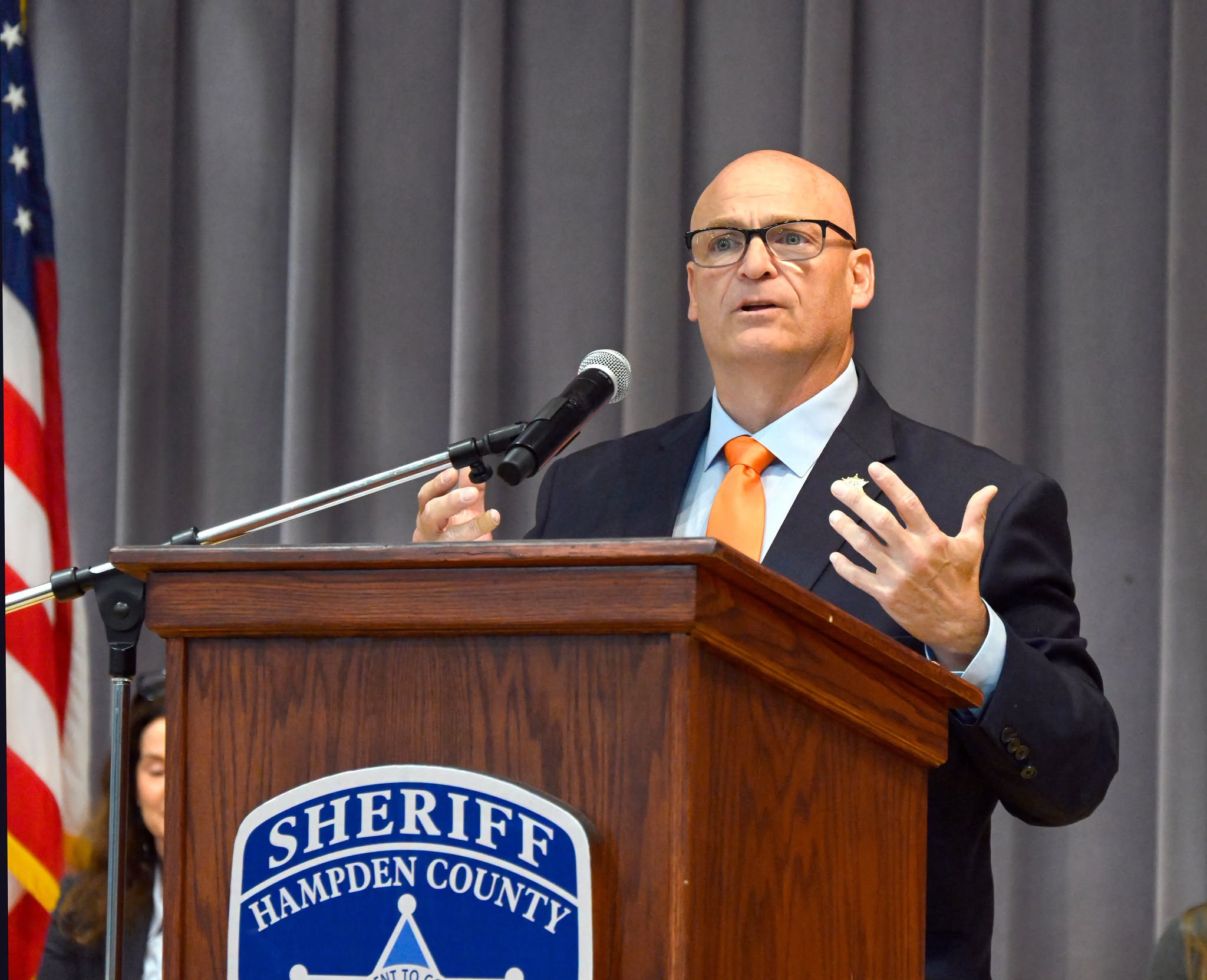 Hampden County Sheriff Nick Cocchi stands at a podium, an American flag to the left.